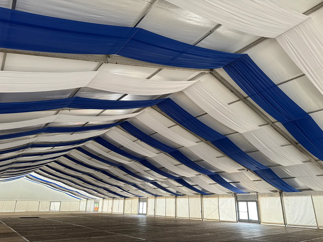Blau-weiße Stoffbahnen im Festzelt als Zelthimmel – klassische Oktoberfest-Dekoration mit Holzfußboden.