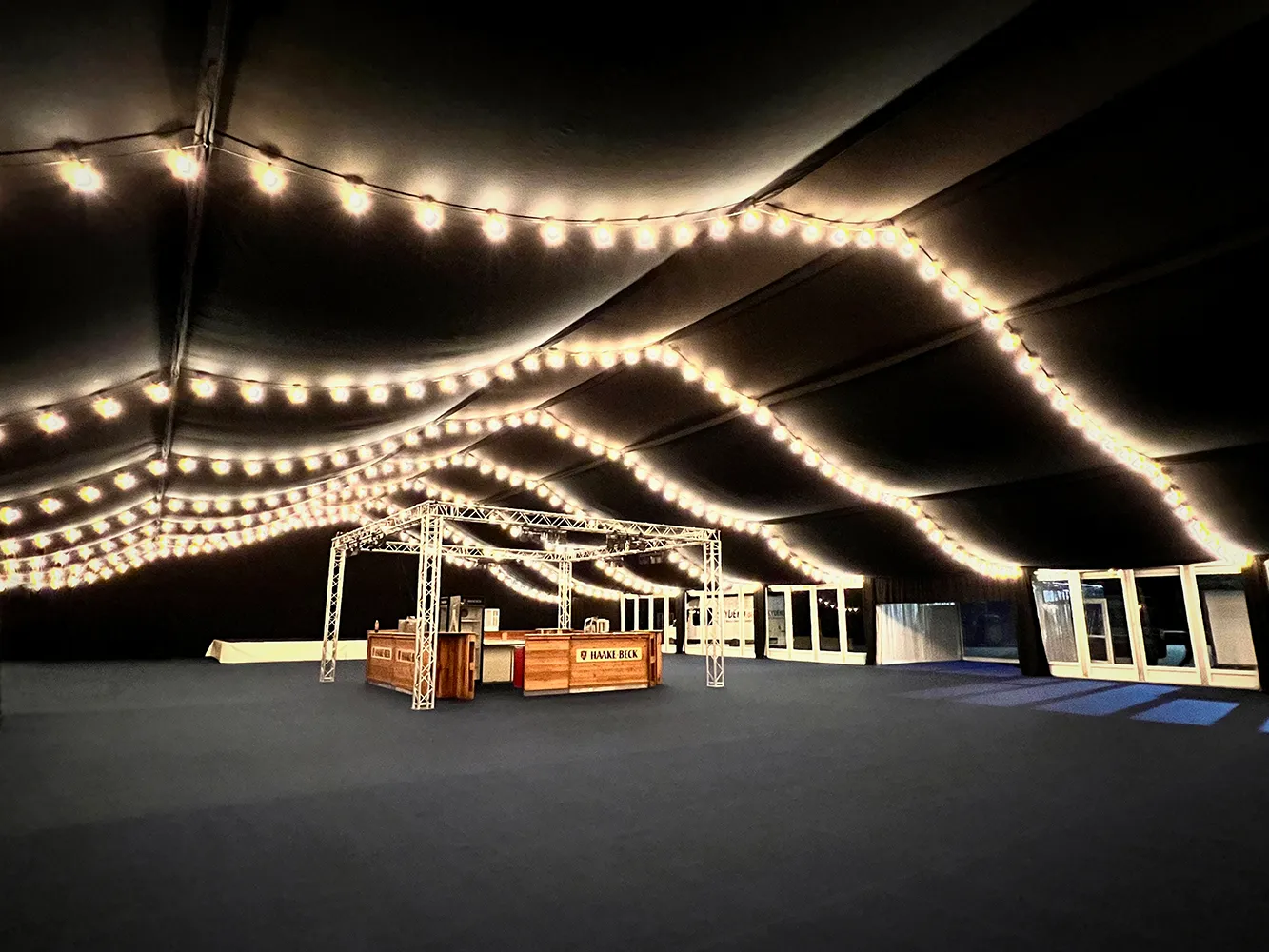 Eventzelt mit schwarzem Zelthimmel, Lichterketten, Seitenverkleidung und dunklem Messeteppich – stimmungsvolle Dekoration von Skydeko.